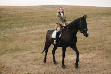 Woman Riding Black Horse Across Open Grassland Fields Near Hillside