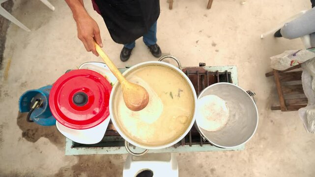 Experienced chef gently stirring traditional Ecuadorian Caldo de Bagre catfish soup in large pot, showcasing authentic latin american culinary heritage and homemade cooking technique