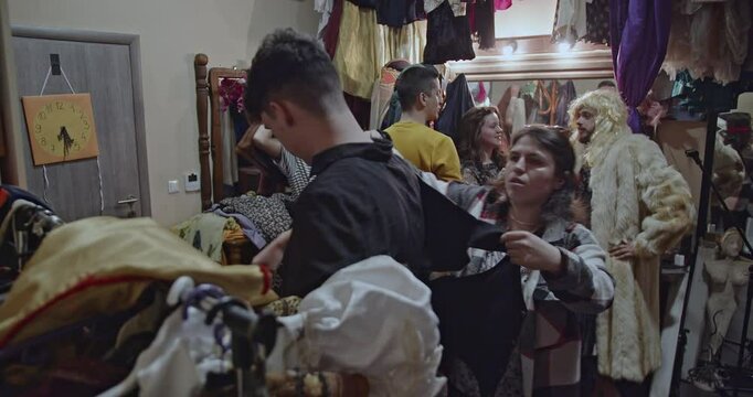Actors prepare backstage, putting on costumes and makeup, in a busy dressing room before a theater play.