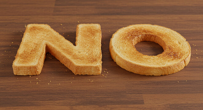 The word no spelled out with toast on a wooden surface with some crumbs scattered around the toast