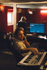 Music producer talking on phone and playing keyboard in recording studio