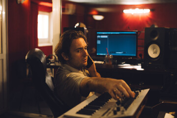 Music producer talking on phone and working on synthesizer in recording studio