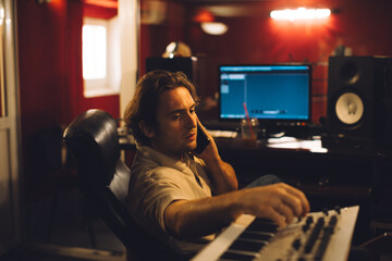 Music producer talking on phone and working on synthesizer in recording studio