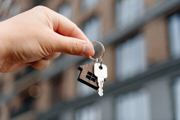 man hand with metal key, keychain in shape of private house, modern brown brick multi-storey...