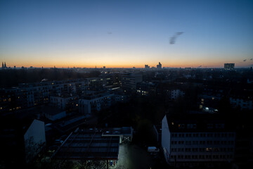 Cologne city skyline at dawn with orange sky and silhouetted city buildings.