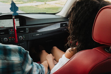 Young couple holding hands in red leather car interior beside navigation display during road trip