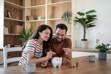 Happy couple saving money together at home putting coins in piggy bank