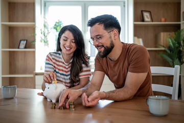 Happy couple inserting coin in piggy bank and calculating savings at home