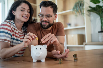 Happy couple saving money inserting coins in piggy bank