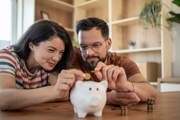 Young couple saving money inserting coins in piggy bank at home
