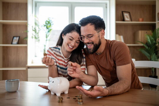 Happy couple saving money together at home using piggy bank
