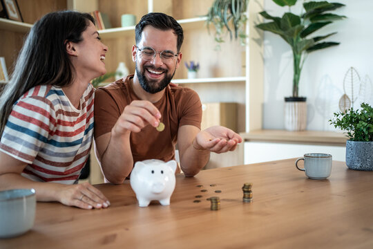 Happy couple saving money together at home putting coins in piggy bank