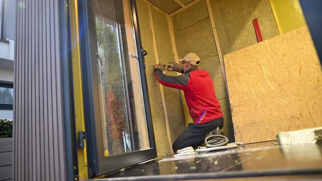 Construction Worker Insulates Walls in Small Cabin During Afternoon Hours