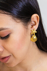 A young Hispanic woman wears a gold earring in her ear against a white background. Colombian beauty...