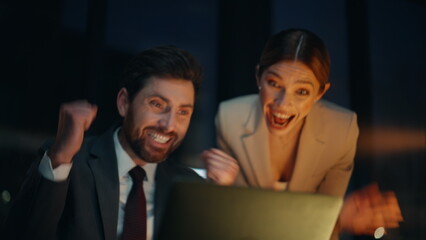 Night office couple rejoicing success winning achievement at computer closeup