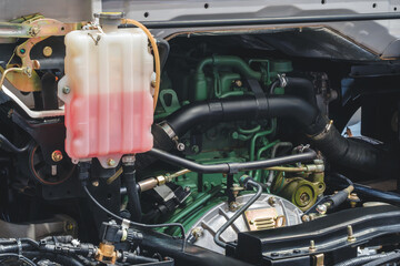 A truck engine with a hose attached to a container of red liquid.