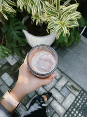 hand holding a glass of iced chocolate with a background of pots and plants