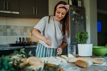 Young caucasian woman making bread dough with rolling pin and flour	
