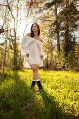 Young woman in a light summer dress standing in a sunny forest clearing