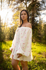 Young woman in a light summer dress standing in a sunny forest clearing