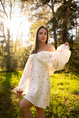 Young woman in a light summer dress standing in a sunny forest clearing