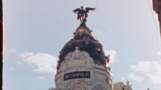 Winged Victory statue stands atop the Metropolis Building dome in Madrid, Spain, a symbol of prosperity and progress, with a clear blue sky and minimal clouds