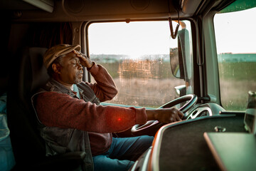 Tired Black truck driver holding head while driving at sunset