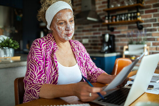 Senior woman doing finances at home while wearing face mask