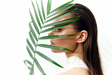 Elegant fashion portrait featuring a model partially hidden behind a palm leaf, showcasing modern...