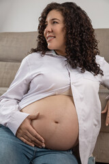 A serene pregnant woman sits comfortably, cradling her baby bump with tenderness and joy, dressed casually, radiating calm and anticipation for the new life to come.