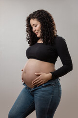 A radiant pregnant woman stands confidently, showcasing her baby bump with pride while wearing a stylish black top and jeans, embodying strength and beauty in motherhood.