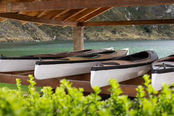 A line of kayaks rests under a wooden shelter by the lake, surrounded by mountains. The image captures a perfect pause before outdoor adventure in a stunning natural setting.

