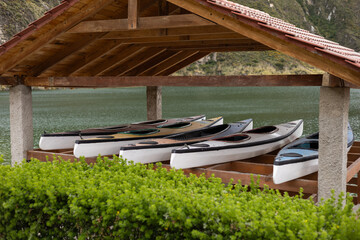 Several kayaks are neatly parked beneath a rustic wooden cabin near a peaceful lake. The scene...