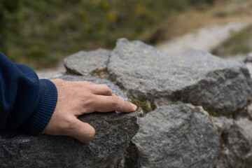 A close-up of a hand gently placed on textured rocks. The image conveys themes of grounding, connection to nature, inner strength, and human presence in the natural world.

