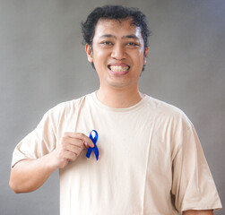 Man showing dark blue ribbon on grey background. Prostate cancer awareness, blue november, men's...
