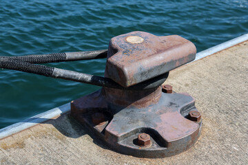 Mooring bollard securing rope on a cement pier by the sea
