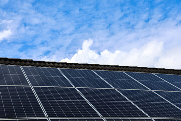 Photovoltaic panels capturing sunlight on a rooftop under a cloudy blue sky