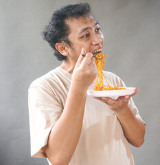 Portrait of handsome asian man eat instant noodle on grey background. He's feel surprise and...