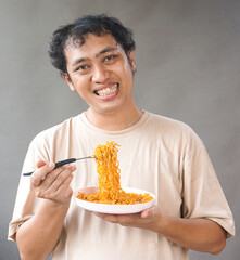 Portrait of handsome asian man eat instant noodle on grey background. He's feel surprise and...