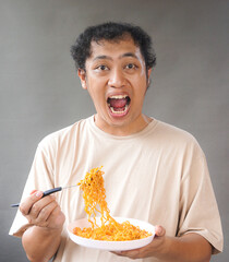 Portrait of handsome asian man eat instant noodle on grey background. He's feel surprise and...