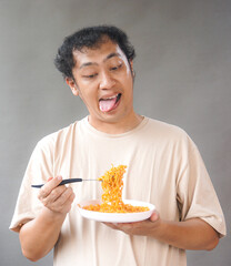 Portrait of handsome asian man eat instant noodle on grey background. He's feel surprise and...