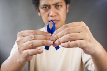 Man showing dark blue ribbon on grey background. Prostate cancer awareness, blue november, men's...