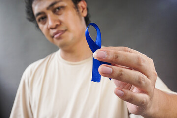 Man showing dark blue ribbon on grey background. Prostate cancer awareness, blue november, men's...