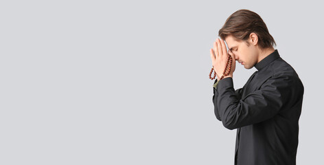 Young priest praying with beads on dark background