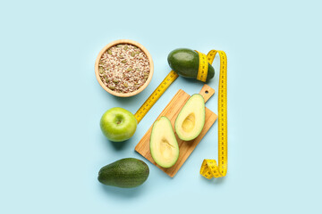 Composition with apple, avocado, bowl of seeds and yellow measuring tape on blue background. Diet...