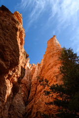 Looking up at dramatic rock spire hoodoo with blue sky and wispy white clouds above, summer vacation exploring in Bryce Canyon National Park, Utah
