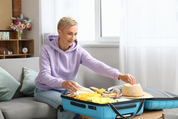 Mature woman packing suitcase at home