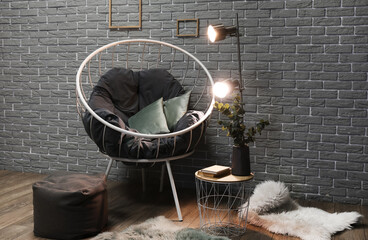 Stylish armchair and glowing lamps on table near grey brick wall