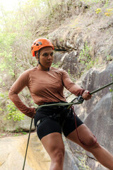 Latin american female athlete rappelling down a steep rock face, demonstrating skill and...