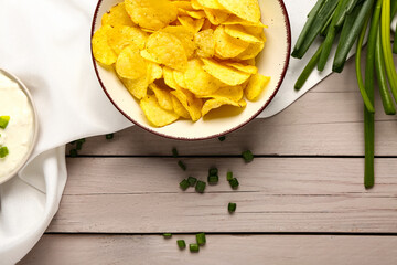 Bowl of tasty sour cream with sliced green onion and potato chips on grey wooden background